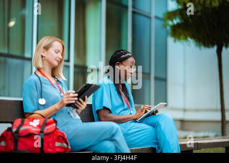 Diverse medical professionals using digital tablets on hospital bench Stock Photo