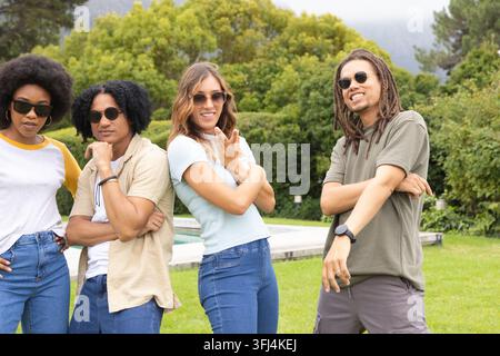 Diverse friends posing together on grassy lawn by pool wearing sunglasses and smartwatch. Outdoor, backyard, grass, water, compa Stock Photo