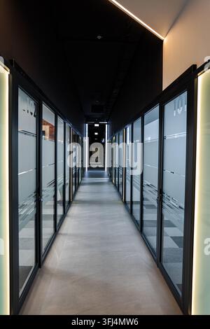 Long empty hallway in a contemporary office building featuring frosted glass walls and overhead lighting Stock Photo