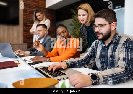 Diverse business professionals collaborating on laptop during meeting Stock Photo