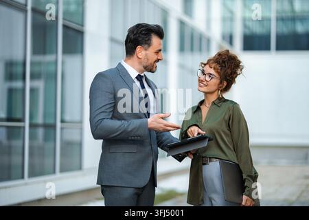 Business colleagues collaborating on a project, using a digital tablet outdoors Stock Photo