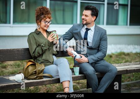 Two business colleagues relaxing during a work break outdoors, smiling and talking Stock Photo