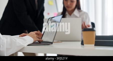 Close up view of employee hands typing on laptop keyboard with charts and graphs displayed on screen during team strategy discussion. Stock Photo