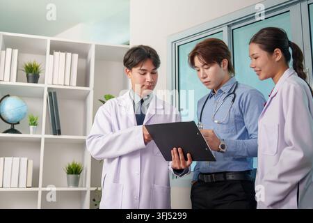 Asian medical team reviewing patient chart clipboard together in clinic office Stock Photo