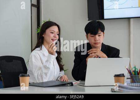 Asian business colleagues discussing strategy over laptop computer during office meeting Stock Photo