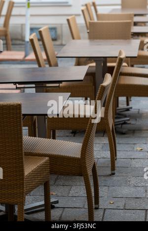 Empty outdoor cafe seating area with woven chairs and tables on a stone pavement. Stock Photo