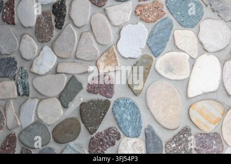 Elegant pebble background with river pebbles decorative wall design in concrete. Modern home decor with natural colorful pebbles as outdoor wall decor Stock Photo