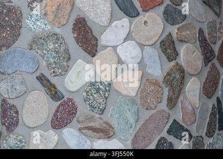 Elegant pebble background with river pebbles decorative wall design in concrete. Modern home decor with natural colorful pebbles as outdoor wall decor Stock Photo