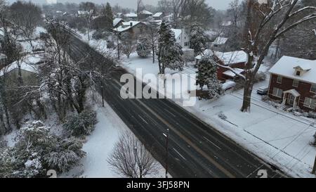 Car driving along snow-covered suburban road in United States. Winter neighborhood with residential houses, trees and fresh snowfall. Calm seasonal at Stock Photo