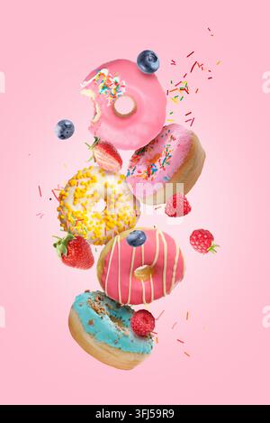 Assorted tasty donuts, fresh berries and sprinkles flying against pink background Stock Photo
