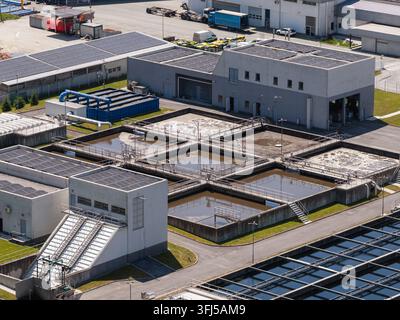 This aerial view shows a wastewater treatment plant with several tanks and treatment areas. Solar panels are visible in the background. Stock Photo