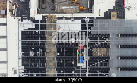 Overhead view of data center under construction with exposed steel framework, scaffolding, building materials and yellow crane on rooftop in Lancaster Stock Photo