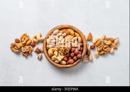 A mix of almonds, cashews, hazelnuts, walnuts, and pistachios in a wooden bowl on a light background. Healthy vegetarian snack concept. Top view, copy Stock Photo