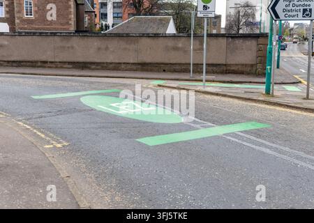 Green LEZ road marking with oval logo at entry point to Dundee low emission zone, alongside directional signs for High School of Dundee and District C Stock Photo