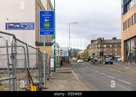 Blue LEZ directional sign with arrow and exemptions notice beside construction hoarding on urban road, with traffic, stone tenements and modern buildi Stock Photo