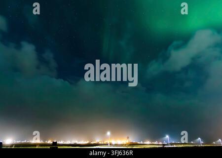 Aurora borealis illuminating the night sky over iceland, with vibrant city lights twinkling in the foreground, creating a magical atmosphere Stock Photo