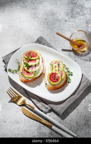 Sweet toasts with fresh figs, cream cheese, thyme, and honey on a gray background. Concept of a delicious dietary appetizer of bruschetta and fruit on Stock Photo