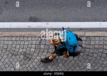 Top view of a female hiker with a large blue backpack walking on a cobblestone sidewalk next to a road, Courmayeur, Aosta Valley, Italy Stock Photo