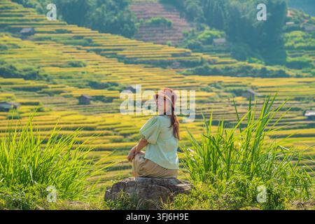 Woman glancing back while seated above blurred rice terrace backdrop, Y Ty, Lao Cai, Vietnam Stock Photo
