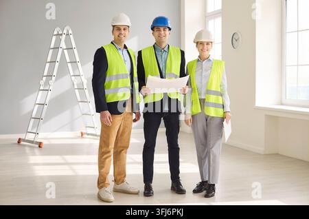 Confident engineers and contractors review blueprints in safety gear indoors Stock Photo
