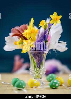 Spring arrangement of yellow daffodils and colorful feathers in a glass vase with decorative Easter eggs. Stock Photo