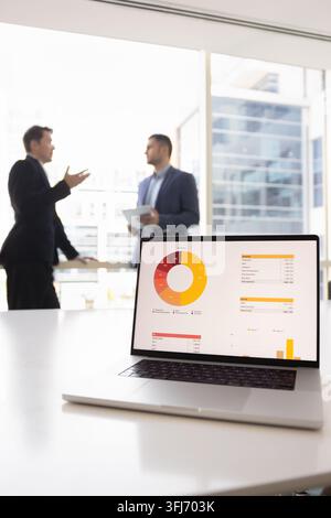 Laptop with chart and colleagues discussing data analysis in office Stock Photo
