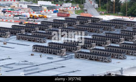 Hundreds of industrial cooling units cover data center rooftop in Lancaster, with active staging area, yellow heavy equipment, and red barriers beyond Stock Photo