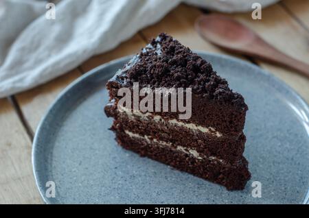 Dark chocolate cake slice, layered with cream. Crumbly topping adds rustic charm. Served on textured gray plate. Soft-focus background enhances desser Stock Photo