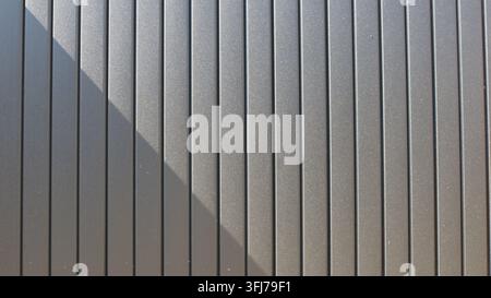 Texture of gray metal siding or vertical-slat blinds. A ribbed, glossy surface with fine sparkles is divided by a diagonal shadow into light and dark Stock Photo