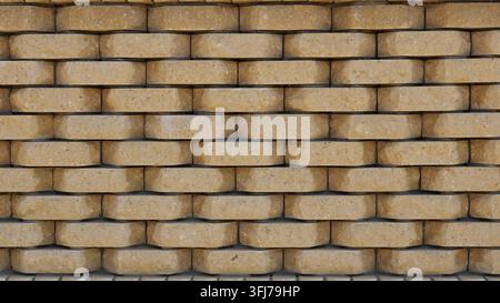 A textured wall made of shaped beige bricks with beveled edges. The three-dimensional horizontal masonry, featuring deep, contrasting shadows Stock Photo