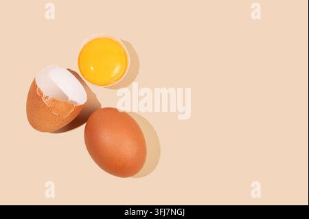 An artistic composition of brown eggs on a yellow background with one cracked egg and a brightly colored yolk. Concept for a banner or advertising lay Stock Photo