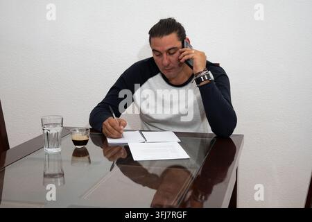 Man writing notes while talking on a mobile phone from his home office Stock Photo