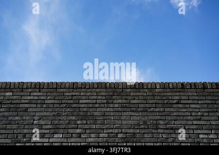Weathered grey brick wall with a clear strip of blue sky Stock Photo