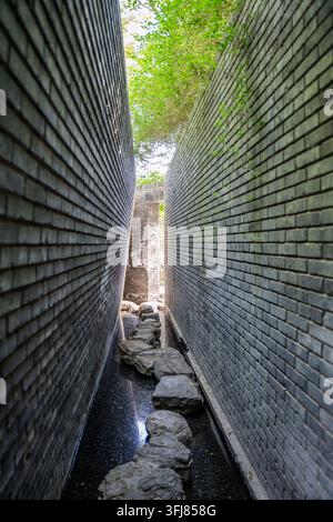Narrow canal path between high gray brick walls Stock Photo