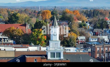 A white clock tower stands tall amid autumn-colored trees in a serene town. Aerial zoom lens, Hagerstown, Maryland. Stock Photo