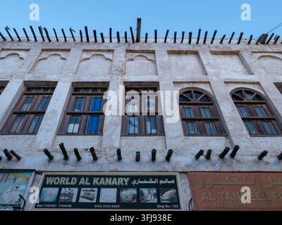 Low angle view of traditional Qatari plaster building facade with wooden beams, arched windows, and shop signs in Souq Waqif. Stock Photo