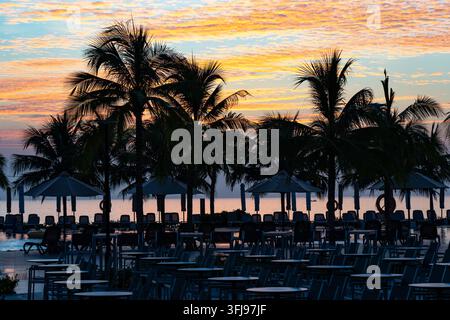 Serene Sunset Over Tranquil Beach with Palm Trees Silhouetted Against the Colorful Sky at Dusk. Stock Photo