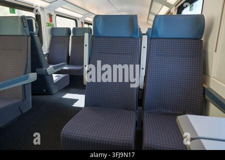 nterior of a modern passenger train carriage featuring rows of blue seats and natural daylight. Clean public transportation background suitable for tr Stock Photo