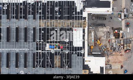 Data center rooftop in Lancaster reveals symmetrical rows of black cooling units on steel grid, with adjacent staging yard and heavy equipment below. Stock Photo