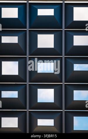 Repetitive geometric grid of square openings in modern architecture creating a rhythmic pattern that frames soft blue sky. Minimal, abstract compositi Stock Photo