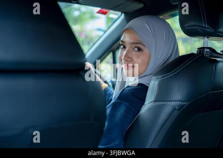 Young woman sitting on a driver's seat in the car and looking at camera over the shoulder Stock Photo