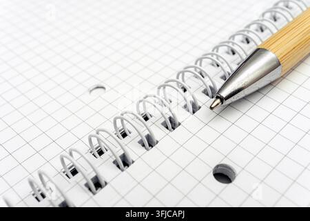 A pen lies on a spiral notebook with graph paper. The notebook is open, showing the blank grid. The setting appears suitable for writing or drawing. Stock Photo