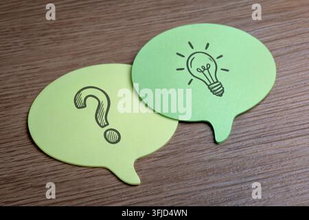 Yellow and green speech bubble notes with drawn question marks and lightbulbs. Brainstorming, problem-solving, FAQ, ideation, solutions concept. Stock Photo