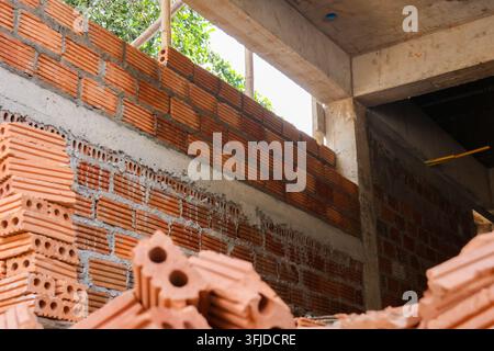 An unfinished red brick building under construction with stacked hollow blocks and concrete frame in daylight Stock Photo