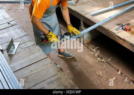 A worker cutting metal bar with power tool in workshop, wearing protective gear and preparing construction material Stock Photo