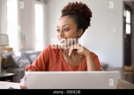 Smiling African woman daydreaming at home office Stock Photo