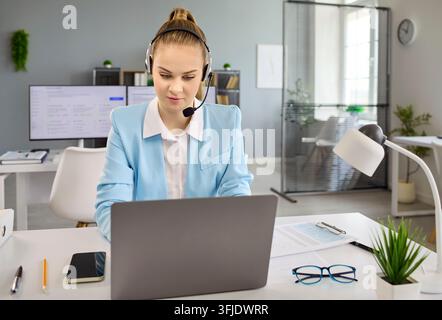Female customer service representative with headset working on laptop in office Stock Photo