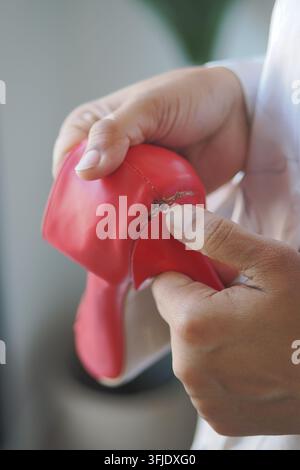 Hands fixing a torn red rubber glove in a workshop setting Stock Photo