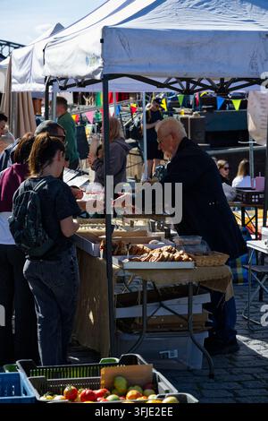 A vendor hands baked goods to a customer at a busy food stall during the Náplavka farmers market. Stock Photo