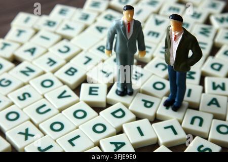 Miniature business figures standing on letter tiles symbolizing communication strategy Stock Photo